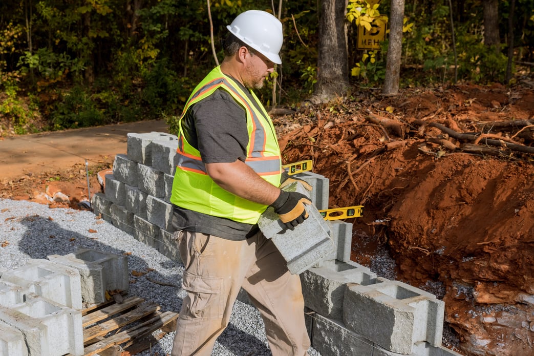 A contractor is constructing a block retaining wall on a construction site while installing a newly constructed wall