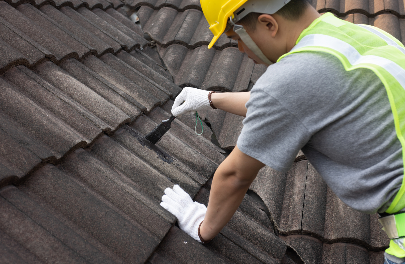 Worker man using waterproof roof coating repair to fix crack of